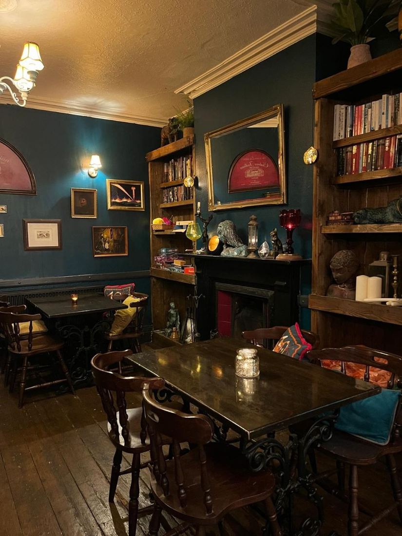 The fireside room in the evening. Its teal walls hold lit pictures and bookshelves, and there are candles on the tables.